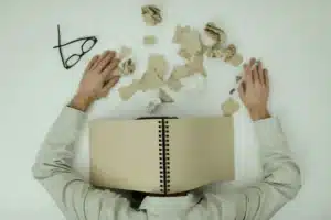 Personne épuisée assise à une table avec des papiers et documents administratifs, symbolisant la charge mentale des aida