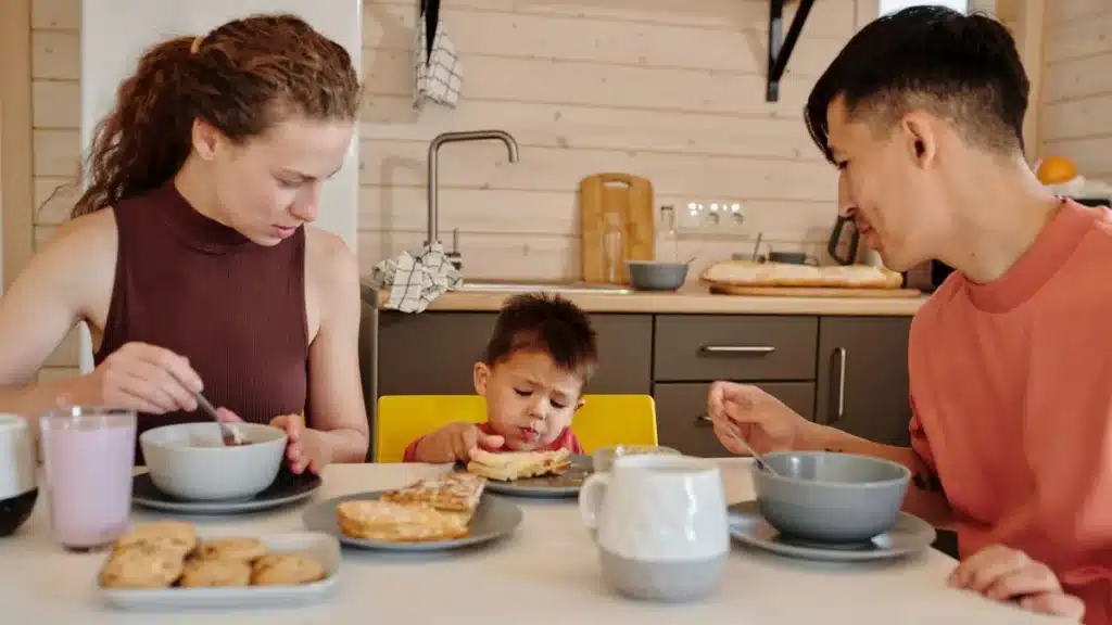 Enfant et adulte à table pendant un repas familial, mains en mouvement, ambiance chaleureuse