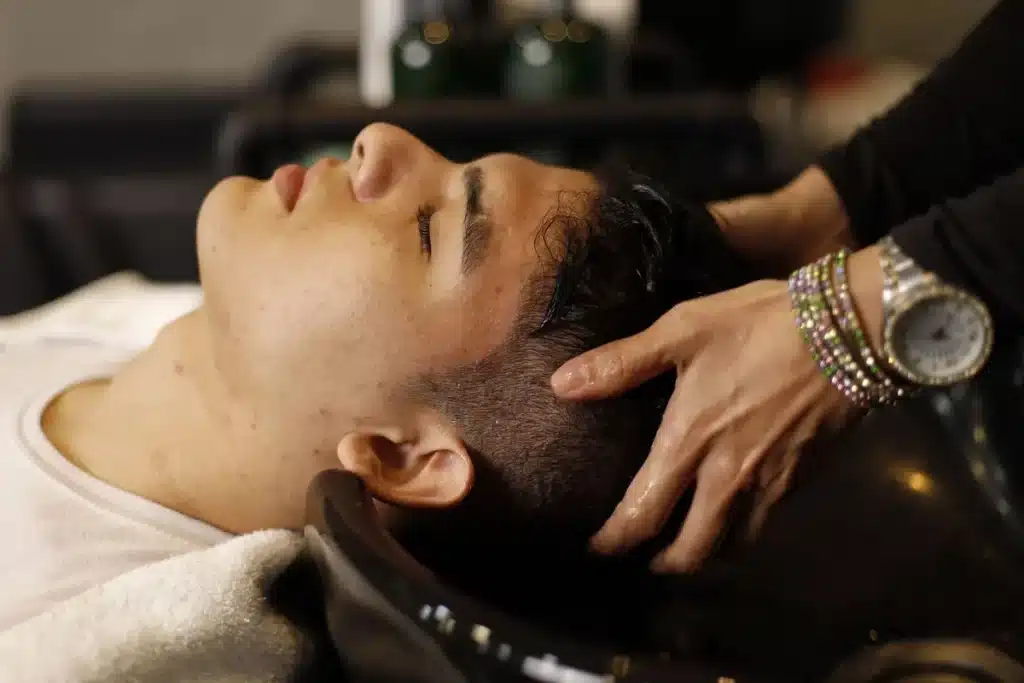 Mains massant le cuir chevelu avec une huile dorée, mouvements circulaires sur racines de cheveux