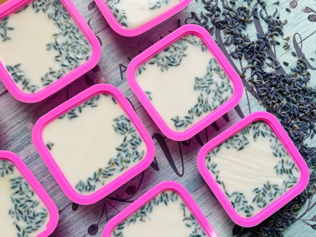 Mains versant des huiles naturelles dans des récipients en verre pour la fabrication artisanale de savon.