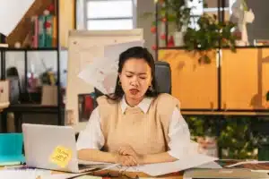 Personne assise à un bureau, épaules tendues, main sur l'abdomen, montrant les effets physiques du stress