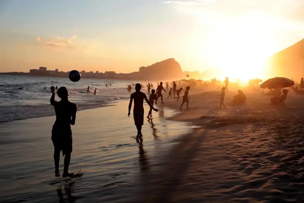 Silhouettes d'enfants jouant sur une plage au coucher du soleil, serviettes et parasol flous