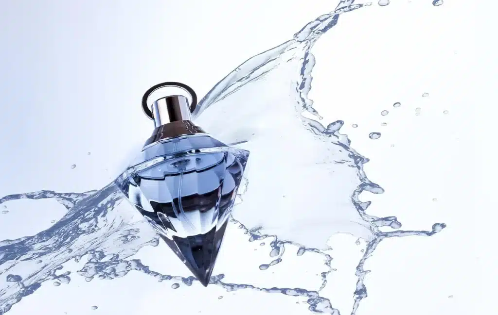 Mains tenant un flacon de parfum de luxe avec un liquide ambré, sur fond intérieur minimaliste