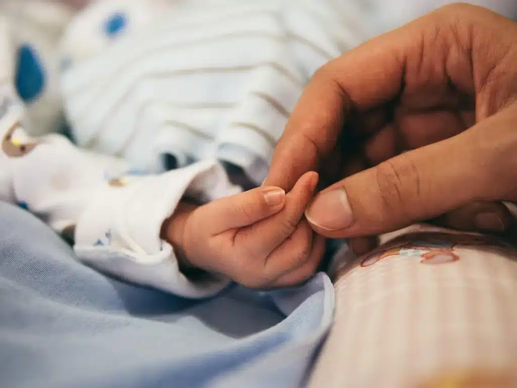 Parent tenant la main d’un enfant près d’une table de jeu, lumière du jour entrant par une fenêtre