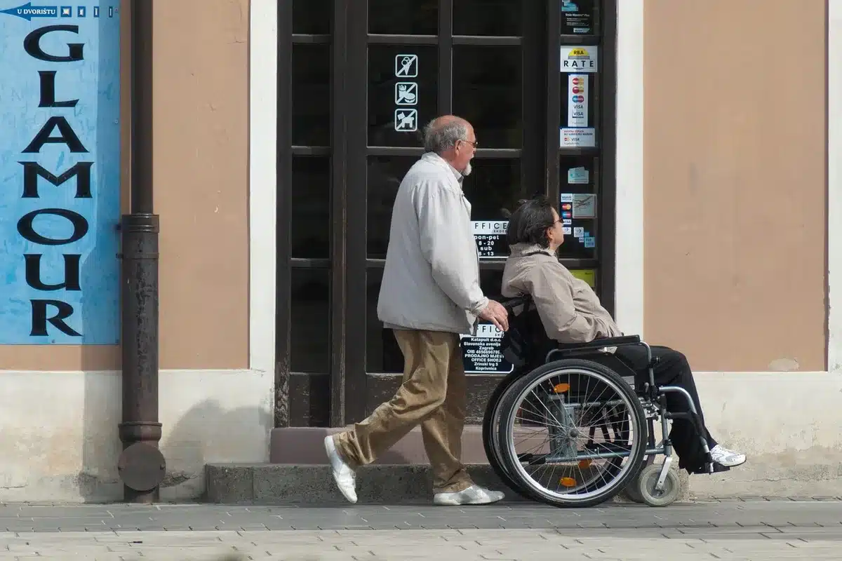 Main d'un aidant guidant une personne en fauteuil dans un couloir accessible